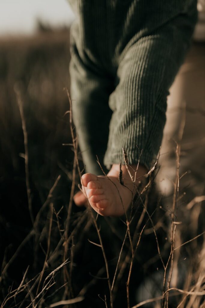 Close-up of a baby's barefoot step on dried grass in a natural, serene setting.